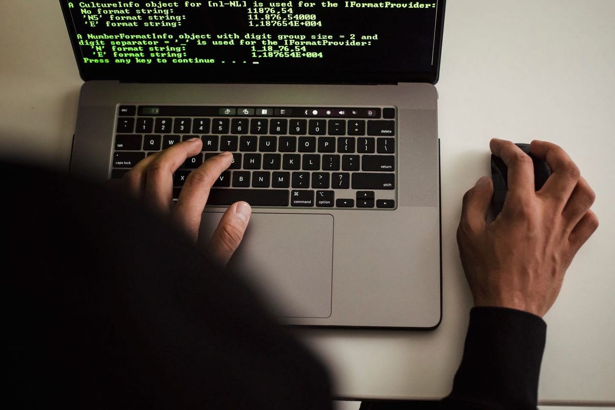Overhead view of two hands typing on a laptop keyboard with terminal output on the screen